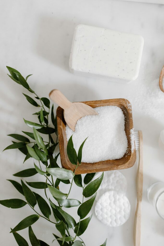 A flat lay of natural bathroom essentials including bar soap and bath salts on a light background.